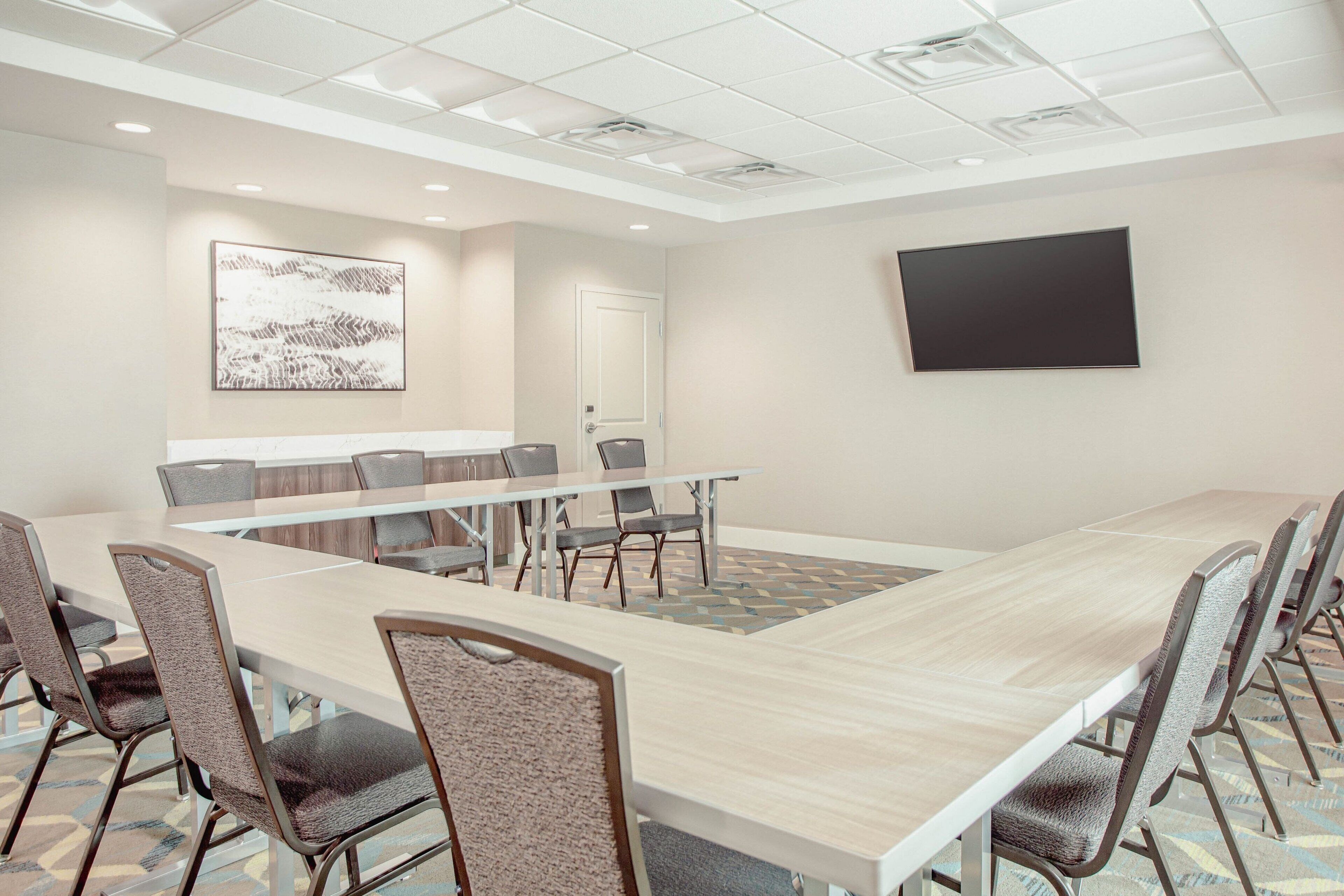 A conference room with a long table, chairs, a whiteboard, and a television on the wall.