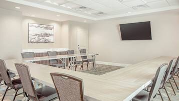 A conference room with a long table, chairs, a whiteboard, and a television on the wall.