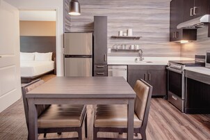 Una habitación de hotel compacta con kitchenette, zona de comedor y cama.
