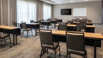 Un salón de conferencias con varias mesas y sillas, una pantalla grande y suelo alfombrado.