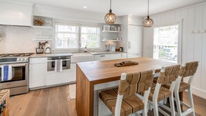 Une cuisine moderne avec des meubles blancs, des appareils en acier inoxydable et un îlot central en bois doté de tabourets de bar.