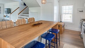 Une cuisine moderne avec un îlot central en bois, des tabourets de bar bleus et une grande fenêtre.