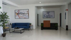 Un moderno vestíbulo de hotel con un sofá azul, una mesa de centro, un mostrador de recepción y un mapa en la pared.