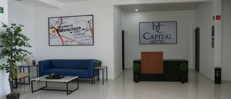 A modern hotel lobby with a blue sofa, a coffee table, a reception desk, and a map on the wall.