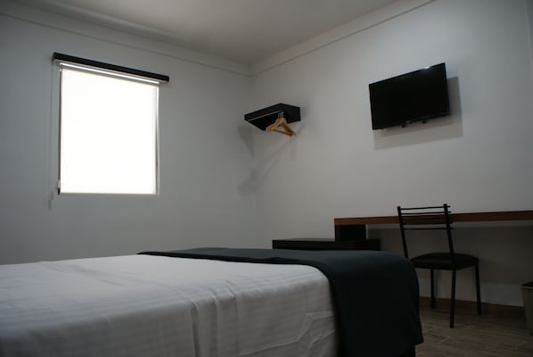 Un dormitorio con cama, escritorio, silla, televisor y ventana.