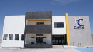 Un hotel moderno con una estructura de dos pisos, un área de estar al aire libre cubierta y un llamativo letrero que dice 'Capital Hotel'.
