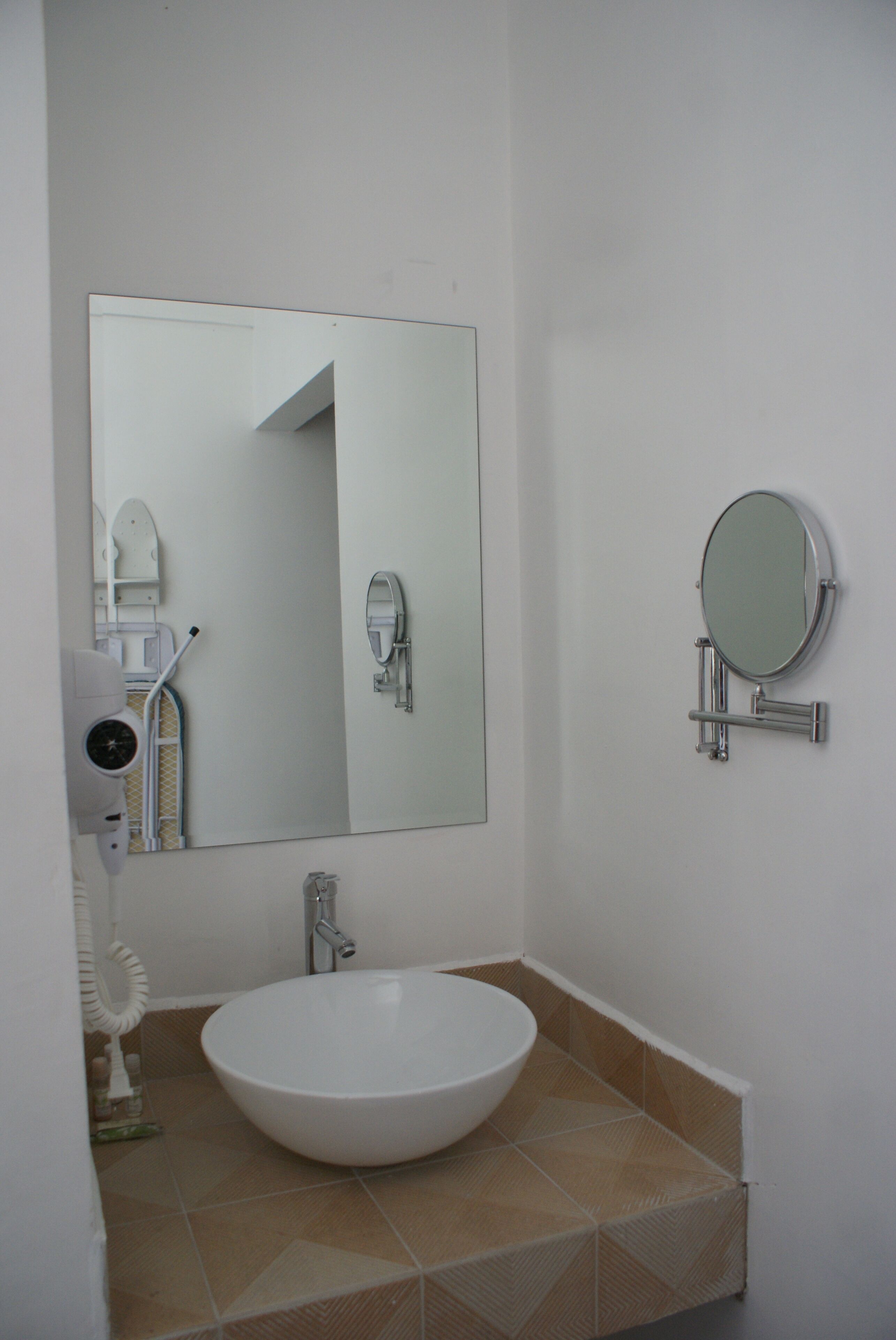 A bathroom with a white sink, a large mirror, and a handheld mirror on the wall.