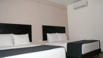 A hotel room with two beds, a headboard, and an air conditioning unit.