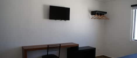 Una habitación pequeña y poco amueblada con un escritorio, una silla y un televisor montado en la pared.