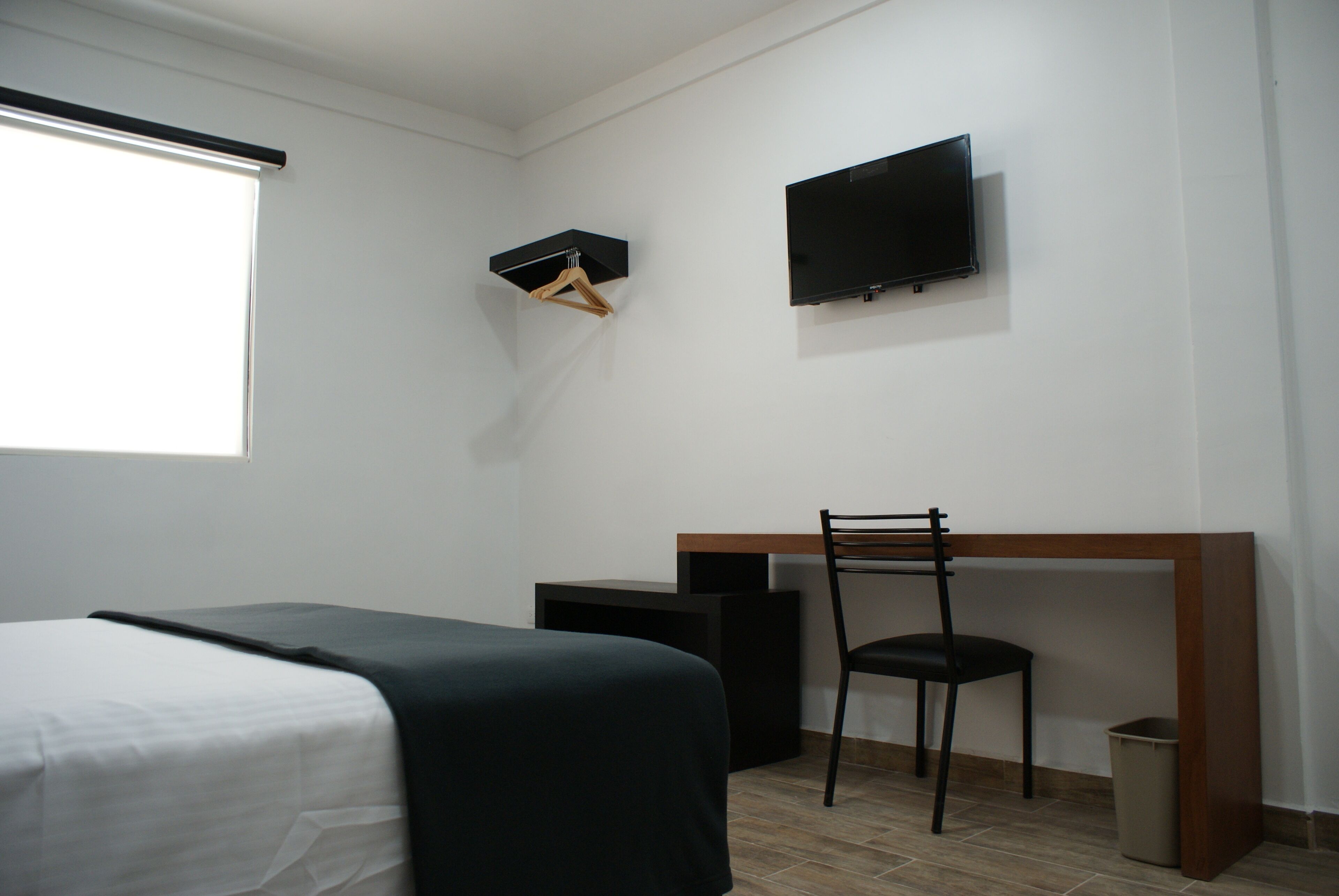 Ett hotellrum med en säng, ett skrivbord, en stol, en tv och ett fönster.