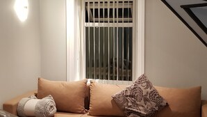Ein gemütliches Wohnzimmer mit einem beigen Sofa, einem zusammengerollten Handtuch und einem floralen Kissen.