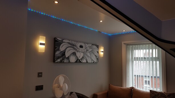 Ein Wohnzimmer mit großem Blumenbild, eingelassenen Deckenleuchten, einem Standventilator und einem Fenster mit Jalousien.