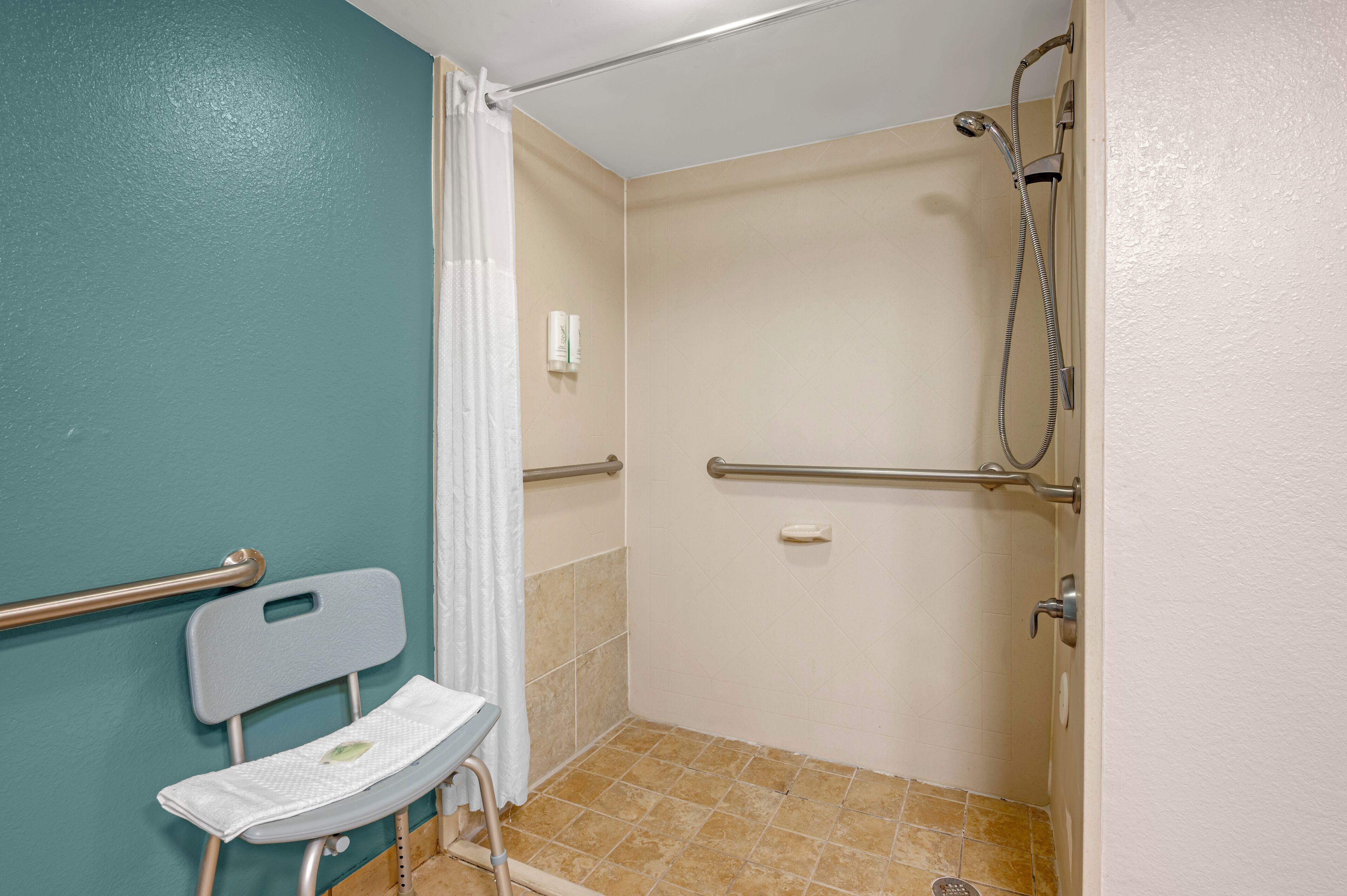 Un baño con ducha, inodoro con asiento de seguridad y pasamanos.