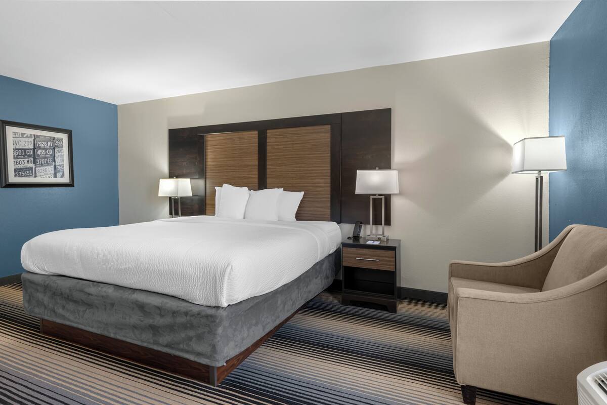 A hotel room with a large bed, two bedside tables with lamps, a chair, and a framed picture on the wall.
