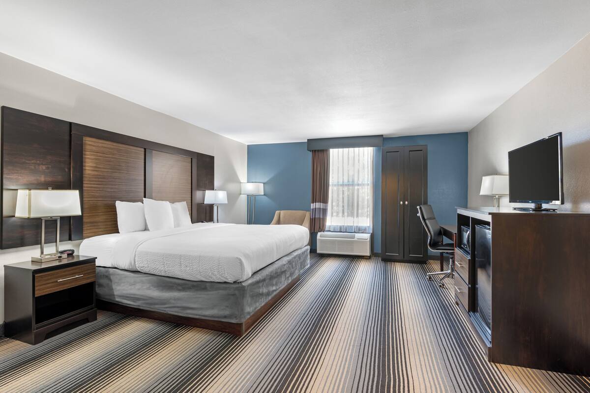 A hotel room with a large bed, a desk, a chair, a TV, and a wardrobe.