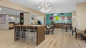 A modern cafe with a central bar area, multiple seating options, and a vibrant wall art display. - Sleep Inn Indianapolis East (Indianapolis)