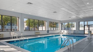 A modern indoor swimming pool with clear glass walls, white tiled ceiling, and multiple lounge chairs around the pool area. - Sleep Inn Indianapolis East (Indianapolis)