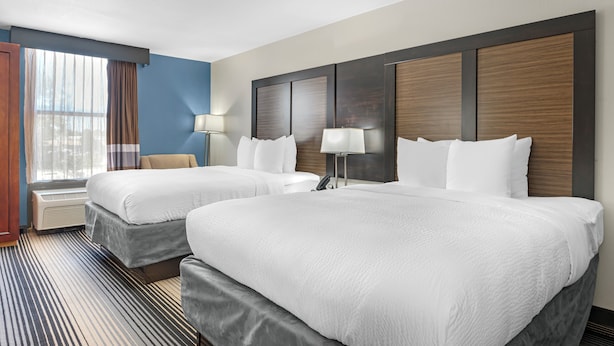 A hotel room with two beds, a large window with curtains, a desk with a lamp, and a wall-mounted phone. - Sleep Inn Indianapolis East (Indianapolis)