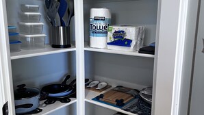 Un placard de rangement bien organisé, avec des étagères où sont rangés les ustensiles de cuisine, les essuie-tout et les boîtes de conservation.