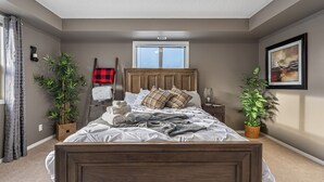 Une chambre à coucher avec un lit en bois, une fenêtre, une table de chevet, une lampe et deux plantes en pot.
