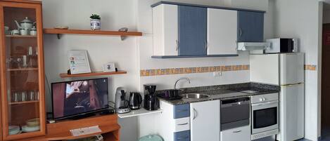 A compact kitchen with white cabinets, a built-in oven, a microwave, and a coffee maker.