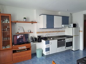 Una cocina compacta con armarios blancos, horno empotrado, microondas y cafetera.