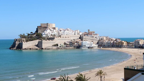 A coastal town with a prominent fortress on a hill, a beach with people, and clear blue skies. - 90 metres from the beach (PENISCOLA)
