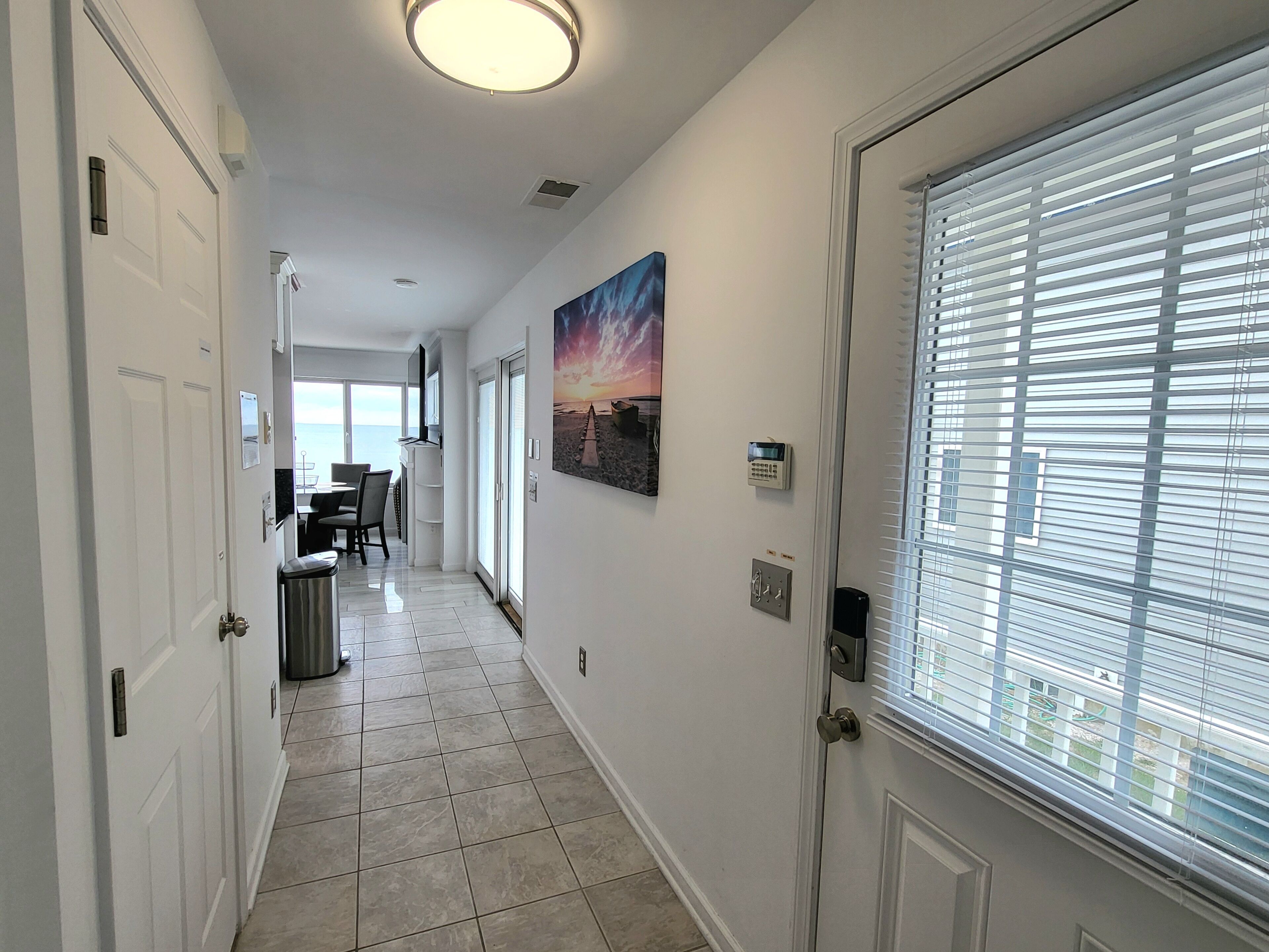 A hallway with a dining area, a painting, and a window with blinds.