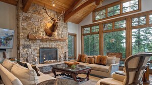 A cozy living room with a stone fireplace, comfortable seating, and large windows offering a view of the forest.