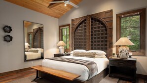 A bedroom with a large bed, wooden headboard, two bedside tables, a bench, and a large mirror.