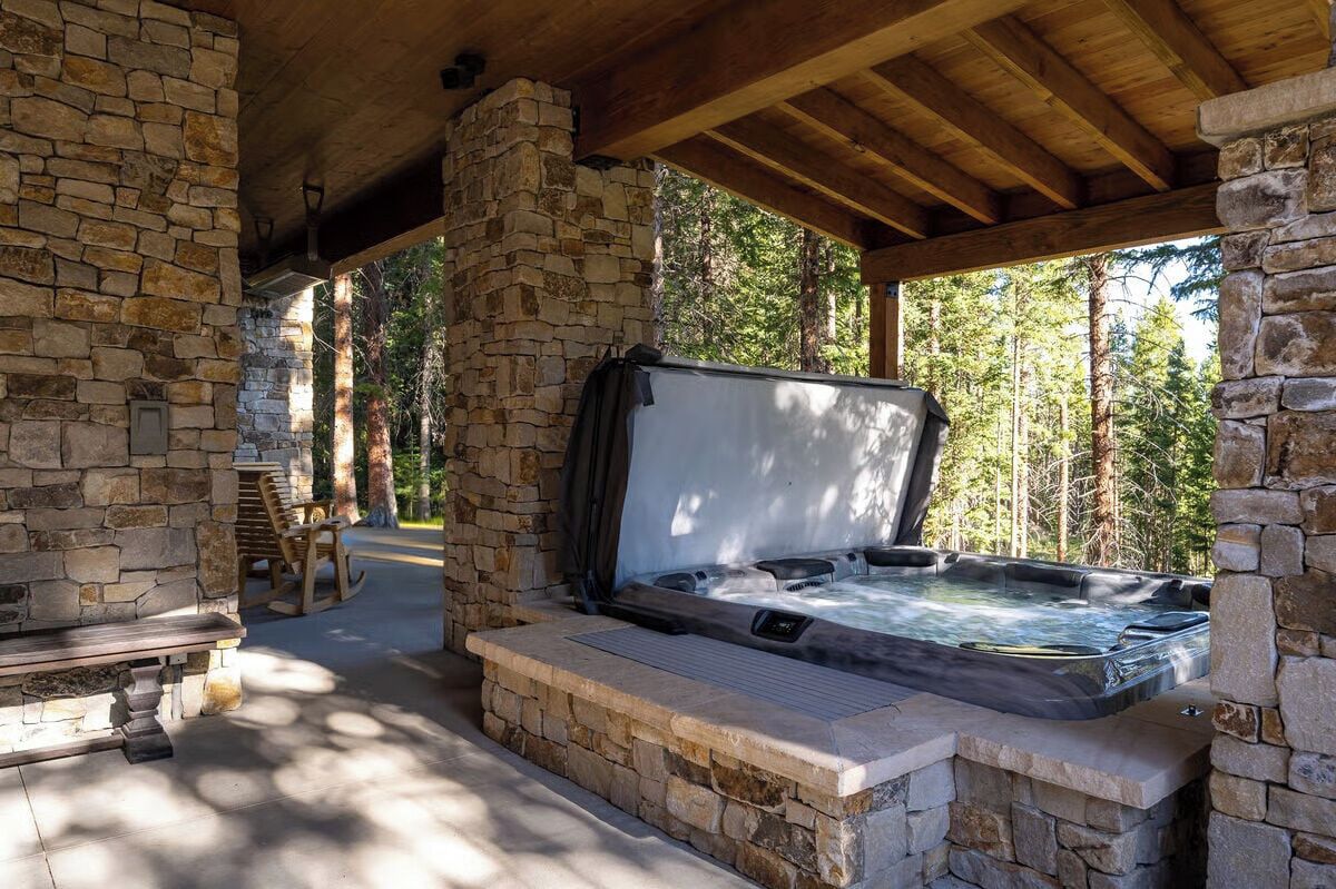 A stone-walled outdoor hot tub area with a wooden bench and a covered seating area.