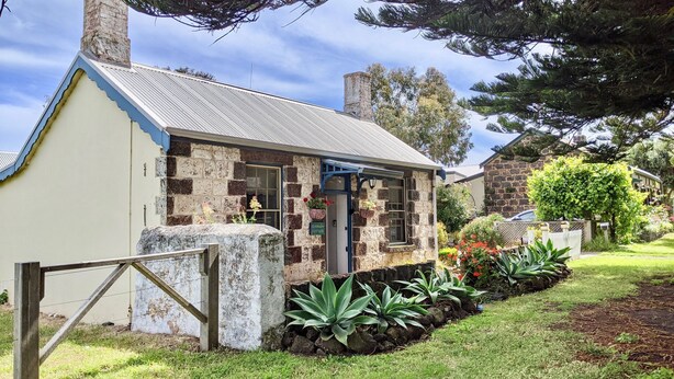 A stone cottage with a blue door, surrounded by a garden with various plants and flowers.