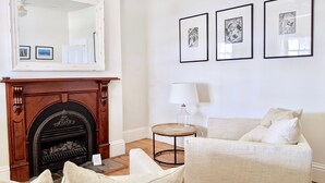 A living room with a fireplace, a sofa, a table, and framed artwork on the wall.