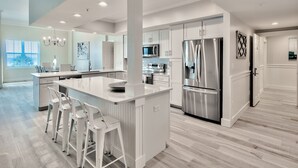 A modern kitchen with white cabinetry, stainless steel appliances, and a central island with bar stools.