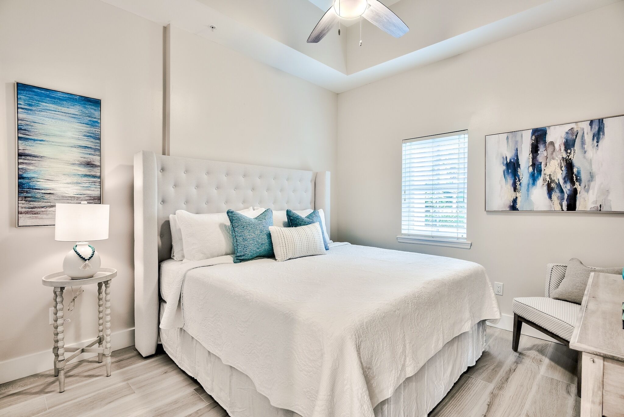 A bedroom with a large bed, a bedside table, a lamp, and artwork on the walls.