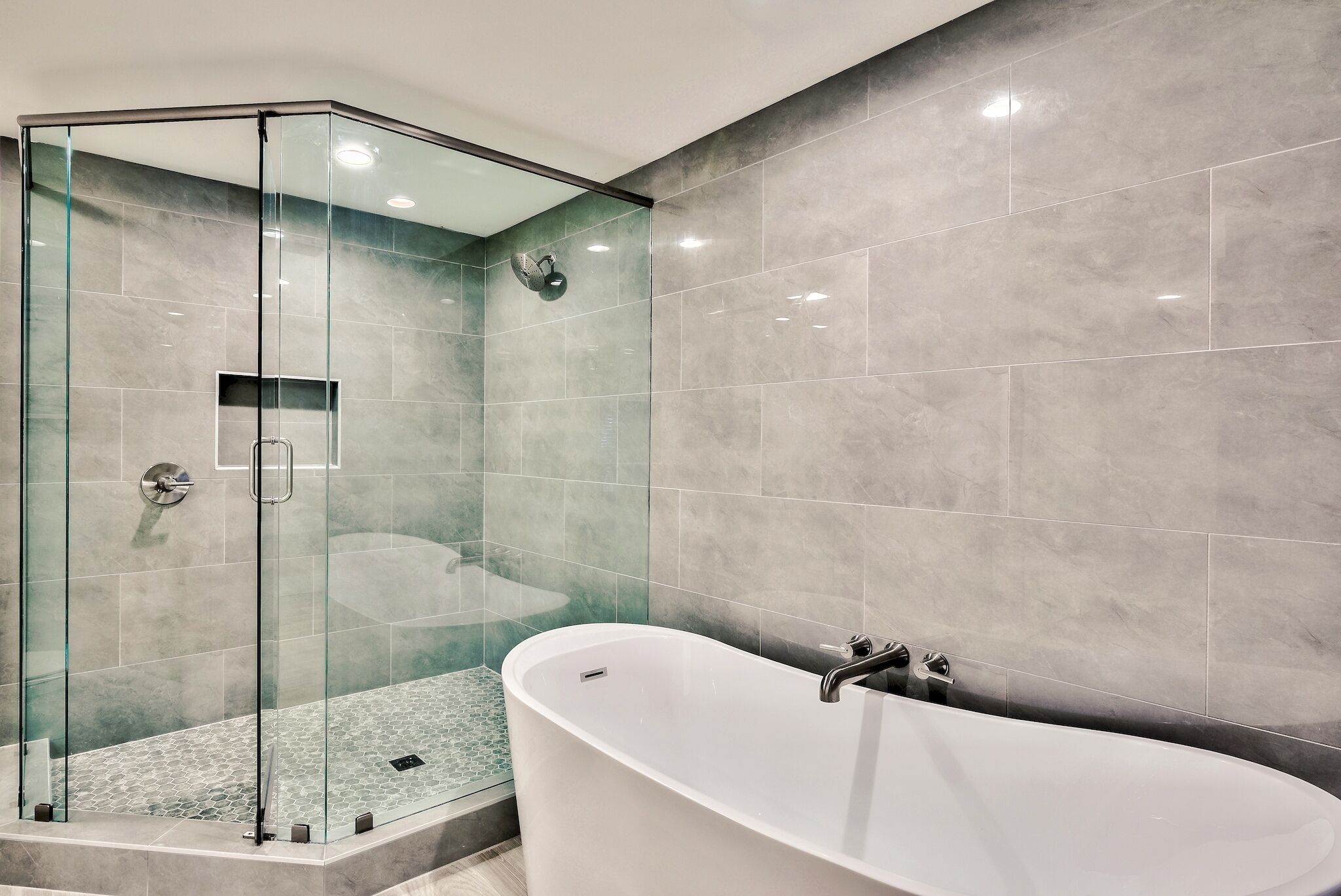 A modern bathroom with a glass-enclosed shower, a freestanding bathtub, and grey marble tiles.
