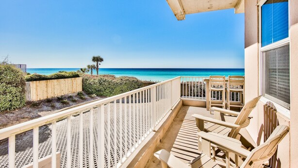 A balcony with a view of the ocean, wooden chairs, and a white railing.