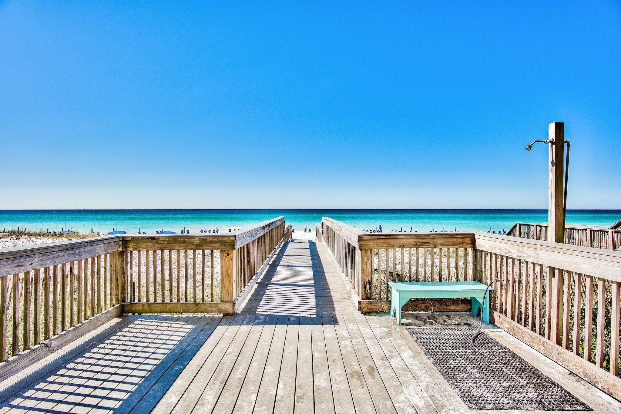 Une promenade en bois menant à une plage, avec un banc et un robinet d’eau.