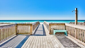 A wooden boardwalk leading to a beach with a bench and a water spigot.
