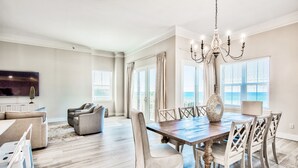 A spacious living room with a large sofa, a dining table with chairs, and a chandelier.