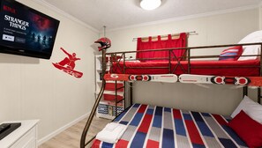 Une chambre avec des lits superposés, un téléviseur diffusant la série « Stranger Things » et un autocollant représentant une planche de snowboard sur le mur.