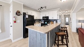 A modern kitchen with white cabinets, a black refrigerator, a microwave, and a stove. There is a bar area with stools. - Summit 108B |3BR,Sunset views, FreeParking (Snowshoe)