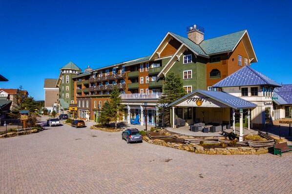 A multi-story hotel with a green and brown facade, a covered outdoor seating area, and a paved driveway. - HH 207: Ski-In/Out | Sunrise Views | Village Steps | Sleeps 4 (Snowshoe)