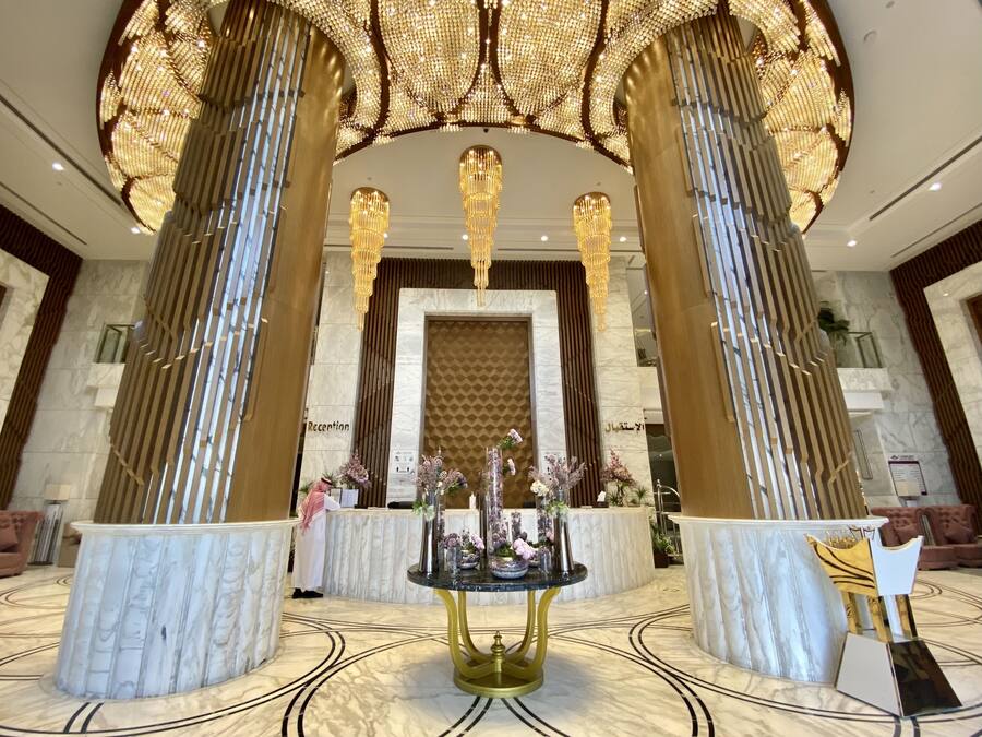 A grand lobby with marble flooring, a reception desk, and a chandelier.