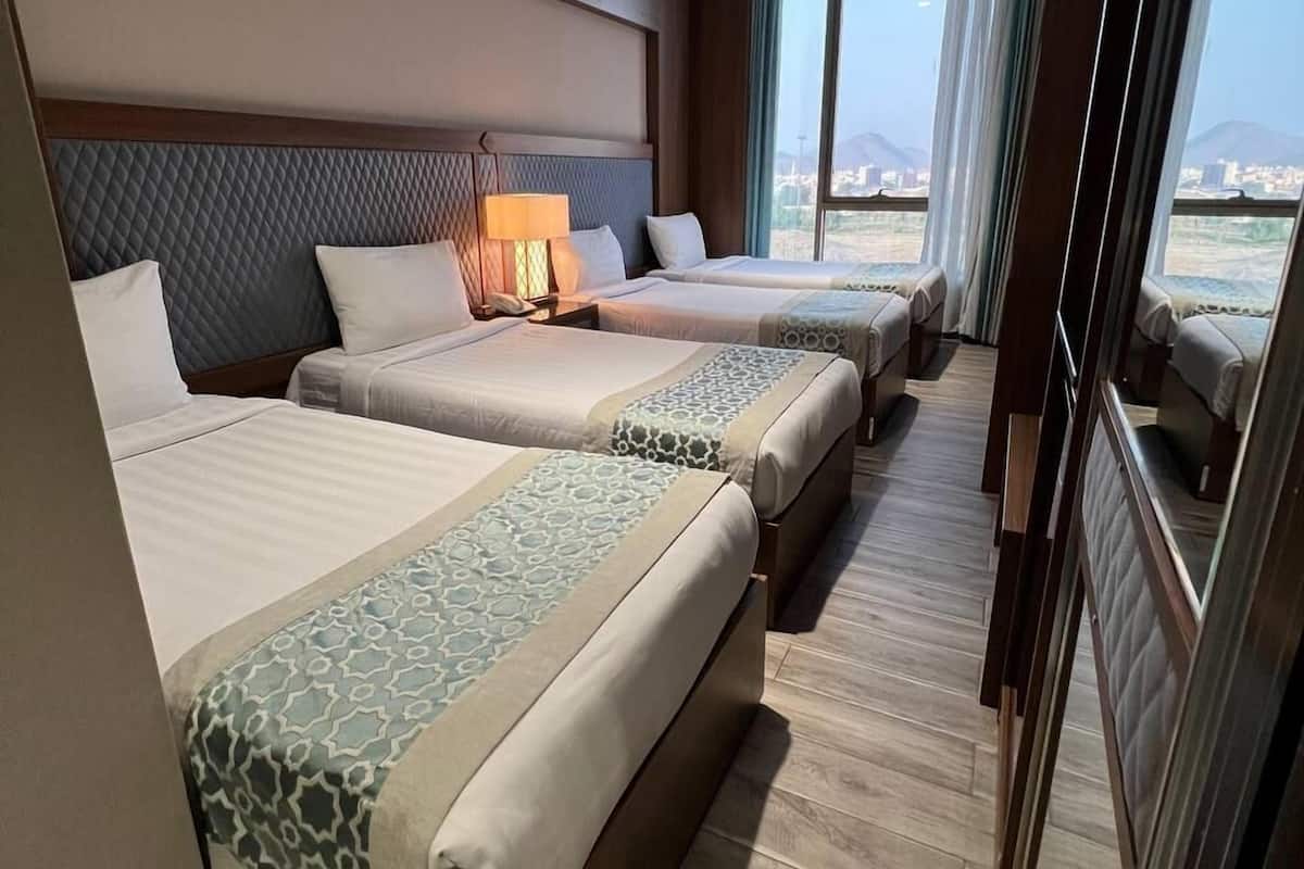A hotel room with two beds, a nightstand, a lamp, and a view of the city.