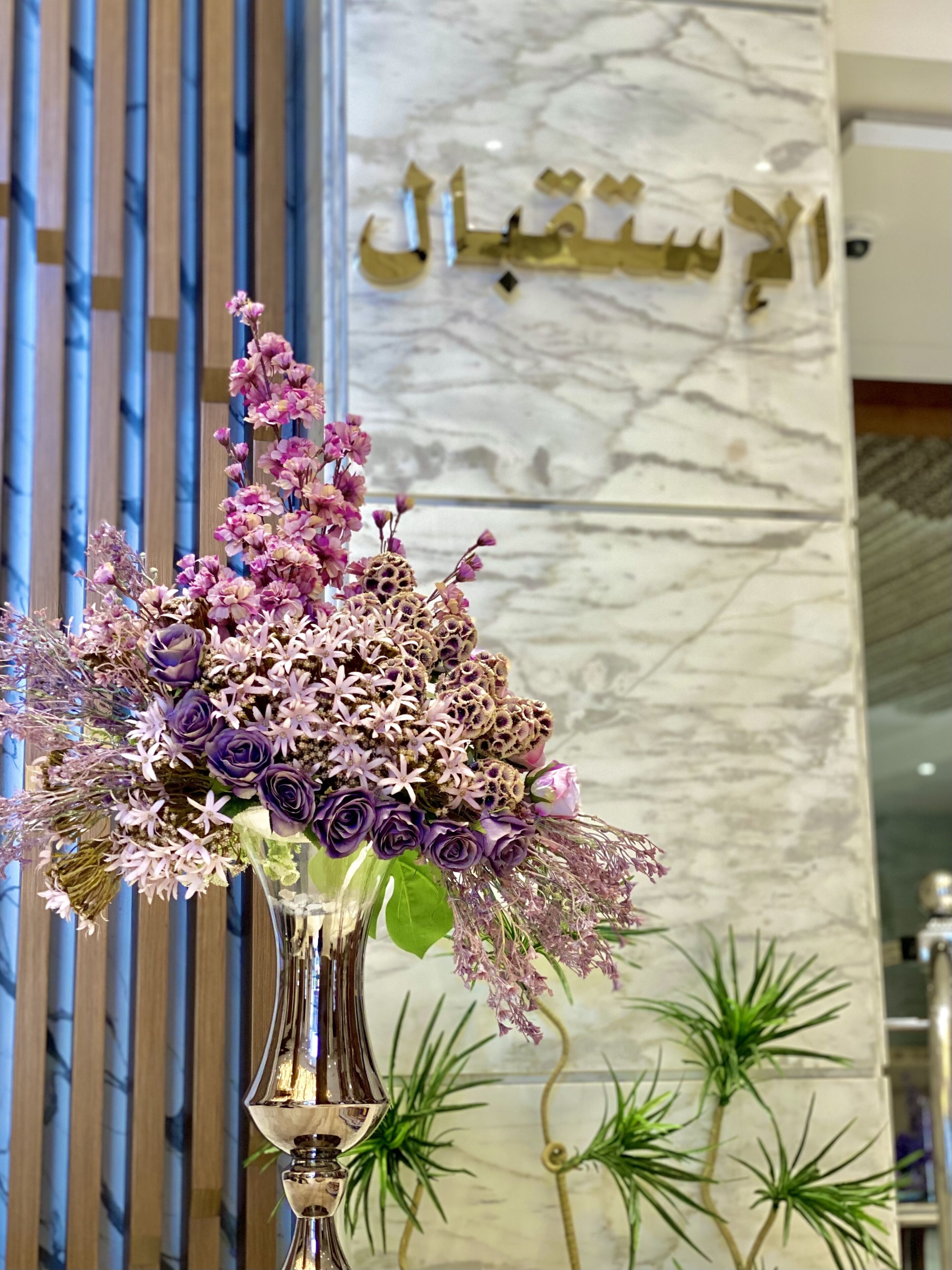 Un bouquet de fleurs dans un vase, pos é sur une table devant un mur de marbre orné d’inscriptions en arabe.