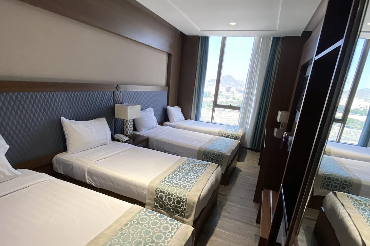 A hotel room with three beds, a large window, and a view of the city.