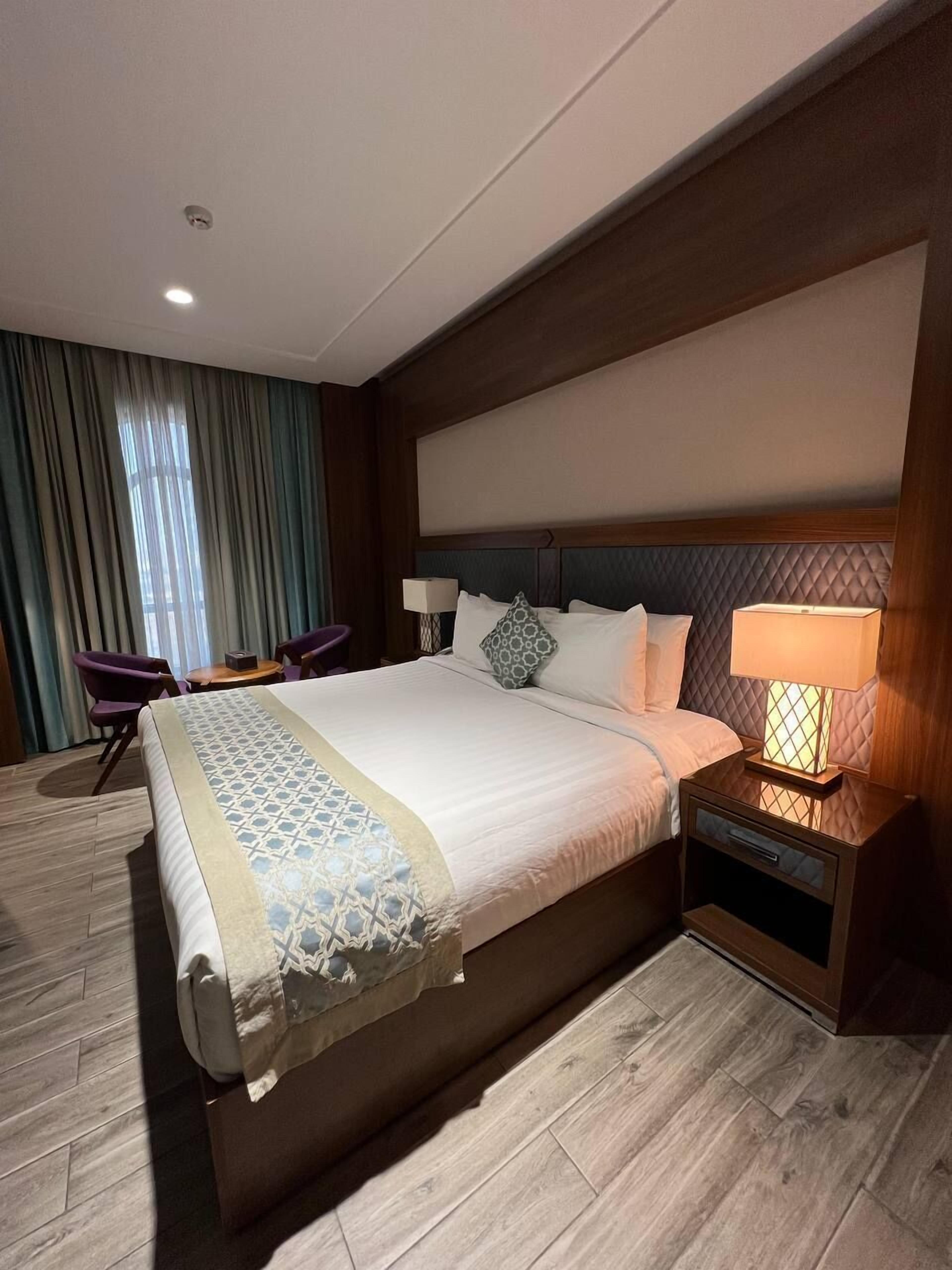 A hotel room with a large bed, two bedside tables with lamps, a chair, and a desk with a chair.