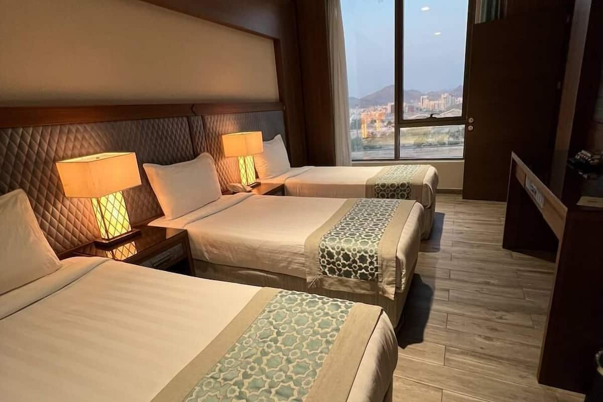 A hotel room with two beds, a large window with a city view, and a wooden floor.