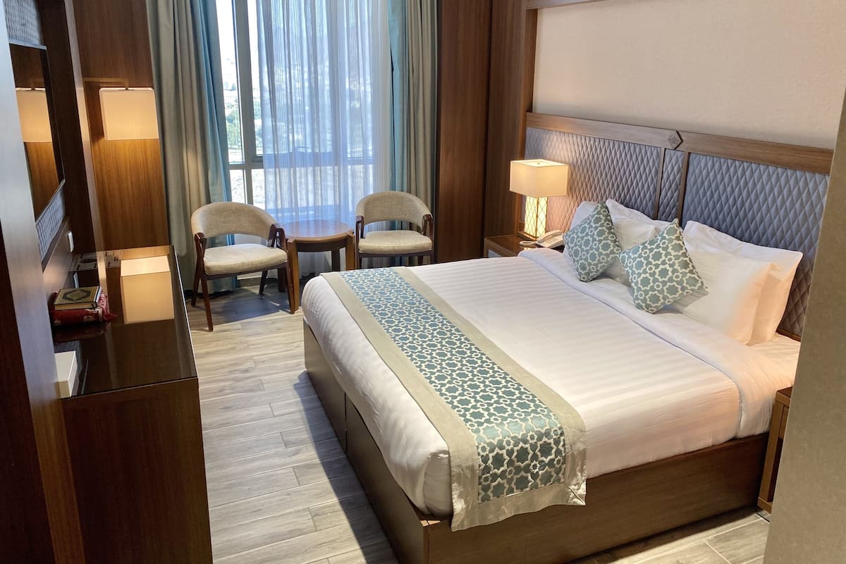 A hotel room with a large bed, two chairs, a small table, and a desk with a lamp.